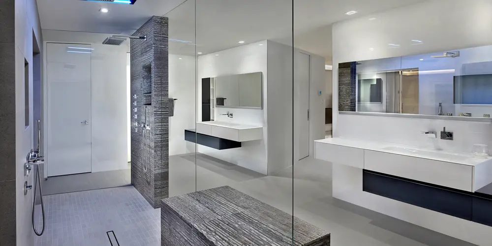 The master bathroom exemplifies luxury and modernity, featuring a spacious walk-in rain shower enclosed in seamless glass, and dual sinks that emphasize functionality and sophisticated design. The room is marked by its use of sleek, minimalist lines and a monochromatic color palette, creating a serene and spa-like atmosphere. High-end materials and strategic lighting contribute to an effortlessly chic aesthetic, offering both style and comfort for daily routines.
