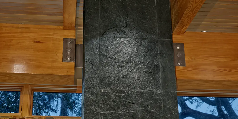The focal point is a dark stone fireplace that exhibits a rugged, natural appearance, emphasizing earthy textures in contrast to the surrounding smooth wooden ceiling. The stone's rich, deep color adds a dramatic tone to the interior design, grounding the space with its solidity and strength.